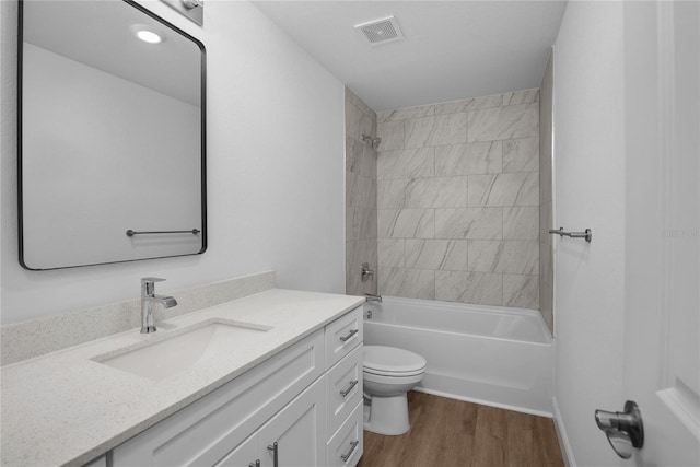 bathroom with visible vents, toilet, wood finished floors, vanity, and  shower combination