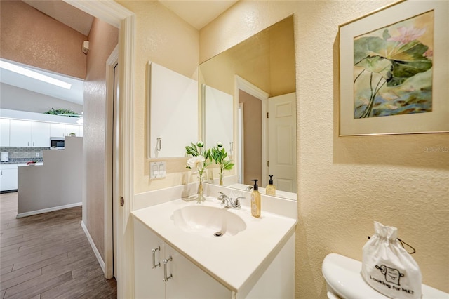 5036 San Rocco Ct, Punta Gorda, FL 33950 - half bath featuring vanity, wood finished floors, decorative backsplash, lofted ceiling with skylight, and a textured wall