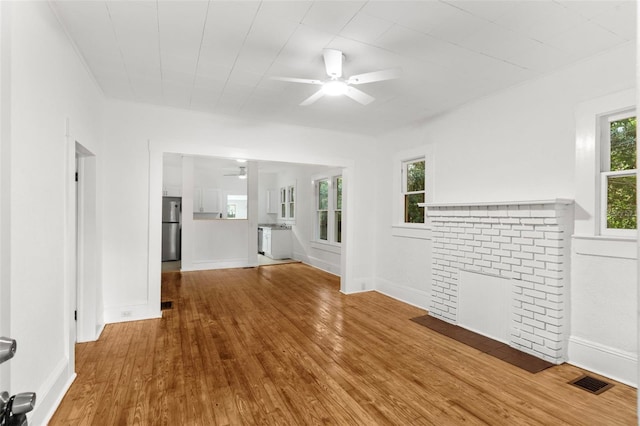unfurnished living room featuring wood finished floors, a ceiling fan, visible vents, baseboards, and a fireplace