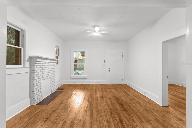 empty room with wood finished floors, a ceiling fan, baseboards, visible vents, and a brick fireplace