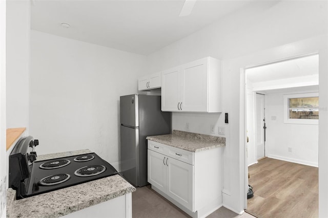 kitchen featuring baseboards, freestanding refrigerator, range with electric cooktop, white cabinets, and light wood-style floors