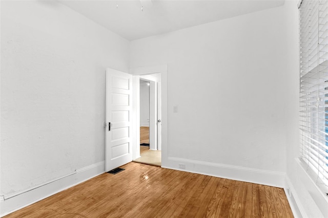 empty room with wood finished floors, visible vents, and baseboards