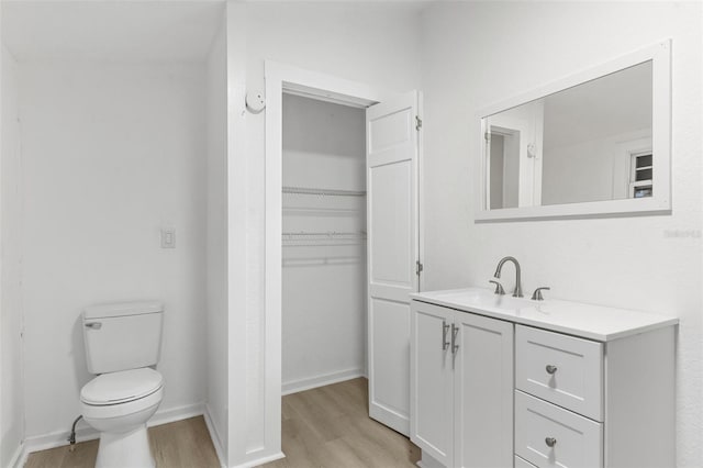 bathroom featuring vanity, wood finished floors, baseboards, a spacious closet, and toilet