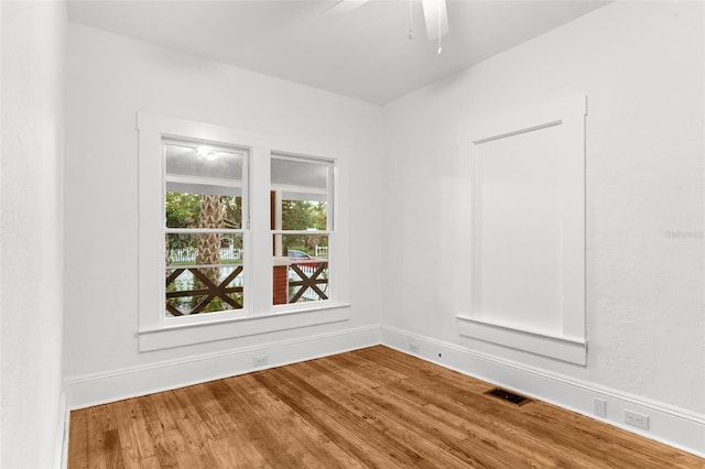 empty room featuring a ceiling fan, wood finished floors, visible vents, and baseboards