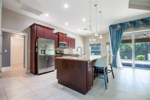 kitchen featuring a kitchen island with sink, a sink, appliances with stainless steel finishes, decorative backsplash, and dark brown cabinets