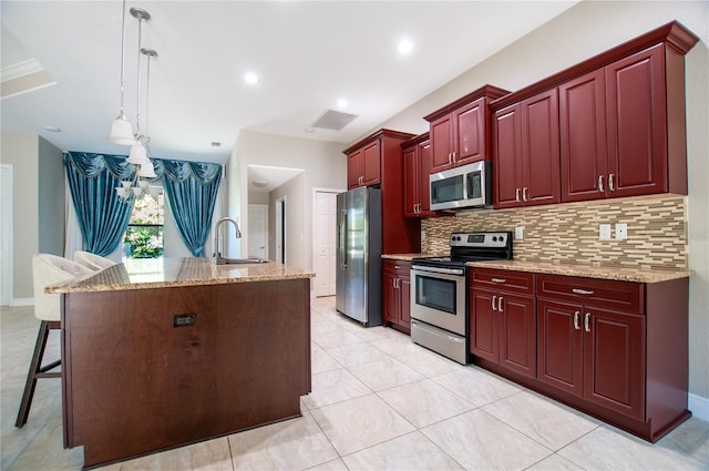 kitchen featuring a sink, stainless steel appliances, reddish brown cabinets, decorative backsplash, and hanging light fixtures