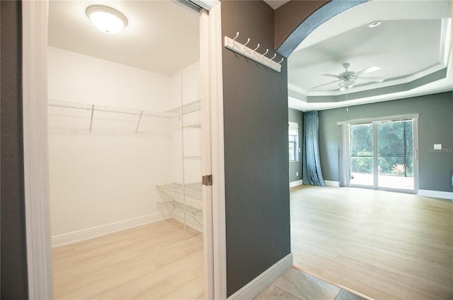 interior space featuring arched walkways, a raised ceiling, a ceiling fan, and wood finished floors