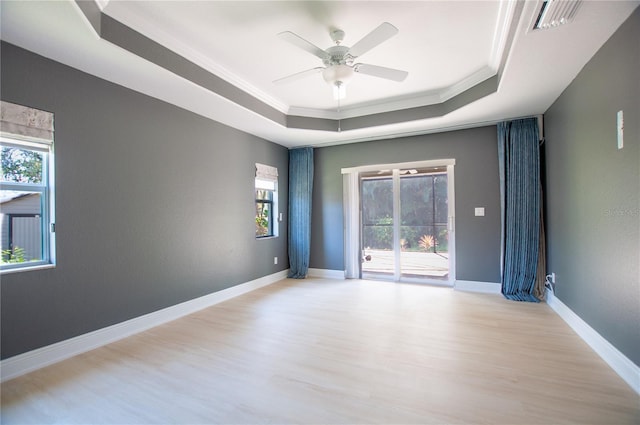 spare room featuring baseboards, light wood finished floors, ornamental molding, ceiling fan, and a raised ceiling