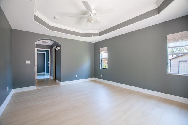 spare room featuring baseboards, a tray ceiling, arched walkways, ceiling fan, and light wood-type flooring