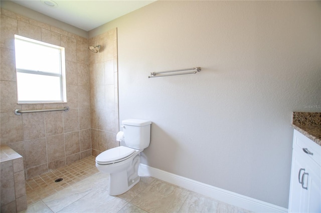 bathroom featuring a tile shower, toilet, vanity, and baseboards