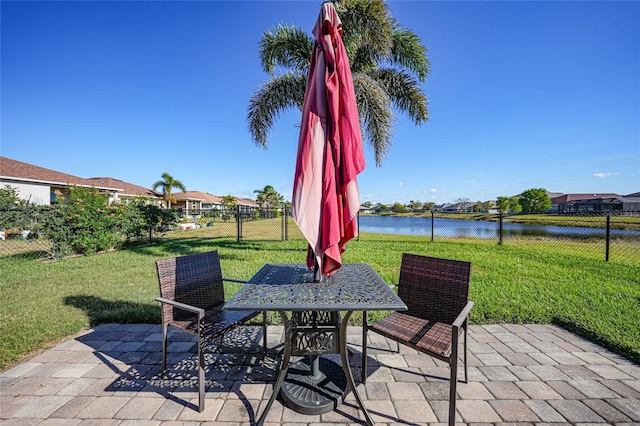 view of patio with a water view, outdoor dining space, and fence