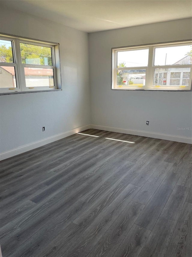 unfurnished room with dark wood-style flooring, a wealth of natural light, and baseboards