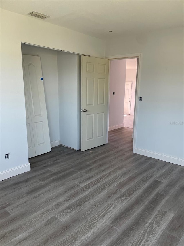 unfurnished bedroom featuring a closet, baseboards, dark wood-style floors, and visible vents