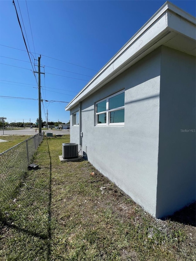 view of property exterior featuring central AC unit, fence, a lawn, and stucco siding