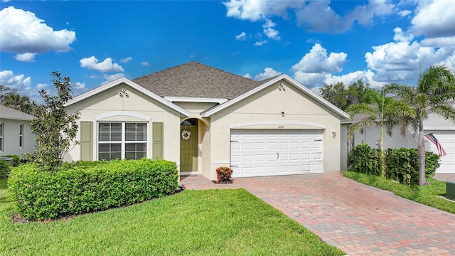 ranch-style house with roof with shingles, an attached garage, stucco siding, a front lawn, and decorative driveway