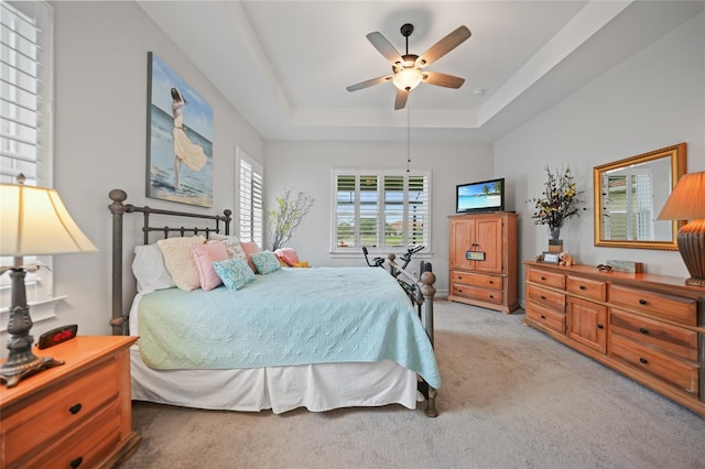 bedroom featuring a ceiling fan, a tray ceiling, and light colored carpet