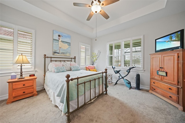bedroom with light carpet, a tray ceiling, and baseboards