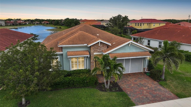 mediterranean / spanish-style house with stucco siding, a tiled roof, decorative driveway, a garage, and a yard