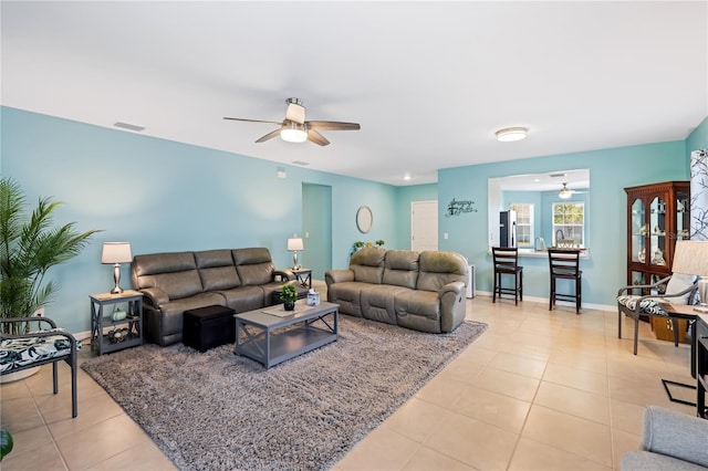 living room featuring light tile patterned floors, visible vents, baseboards, and a ceiling fan