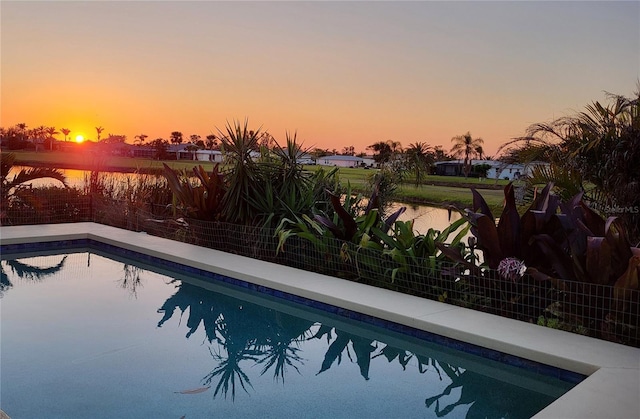 pool at dusk featuring a fenced backyard and a water view