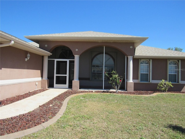entrance to property with a lawn, a shingled roof, and stucco siding