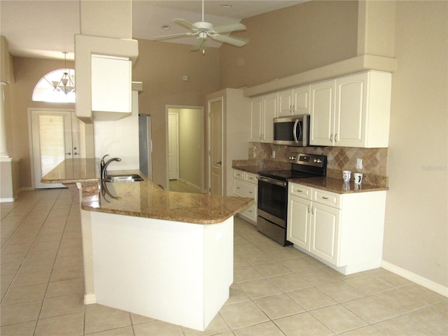 kitchen featuring a sink, light tile patterned floors, stainless steel appliances, ceiling fan, and dark stone counters