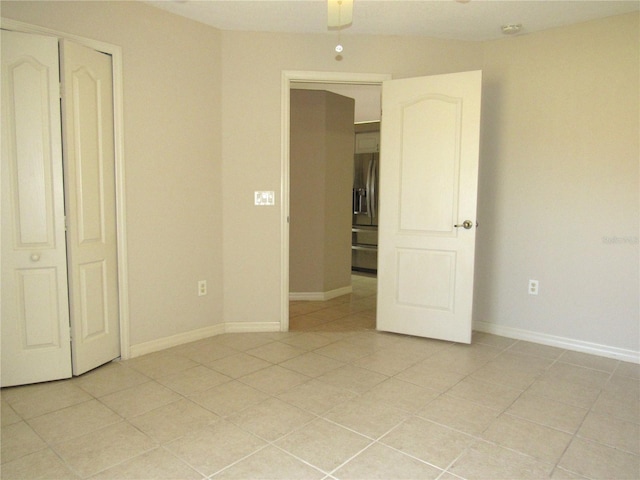 unfurnished bedroom featuring stainless steel fridge with ice dispenser, baseboards, and light tile patterned flooring