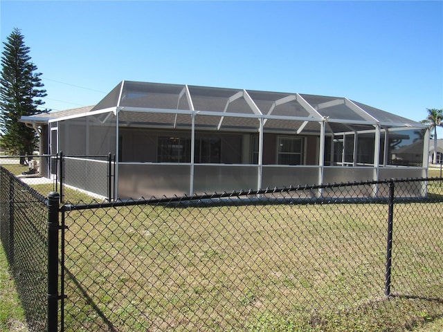 rear view of property with glass enclosure, fence, and a yard