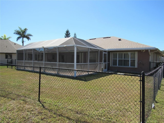 rear view of property with glass enclosure, stucco siding, fence, a shingled roof, and a lawn