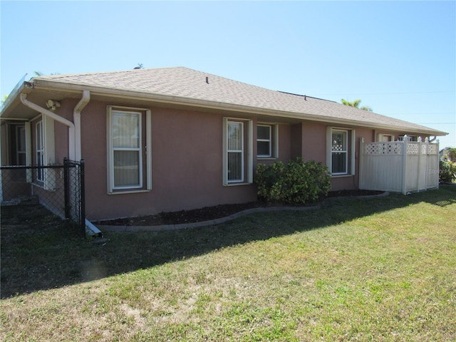 view of front facade with stucco siding, fence, a front lawn, and roof with shingles