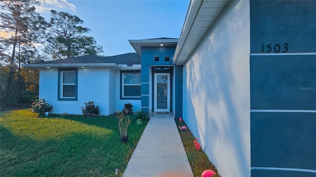 doorway to property with a shingled roof, stucco siding, and a yard