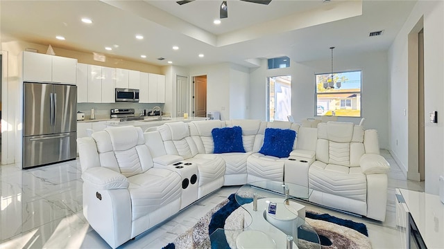 living room featuring marble finish floor, a tray ceiling, recessed lighting, and a ceiling fan