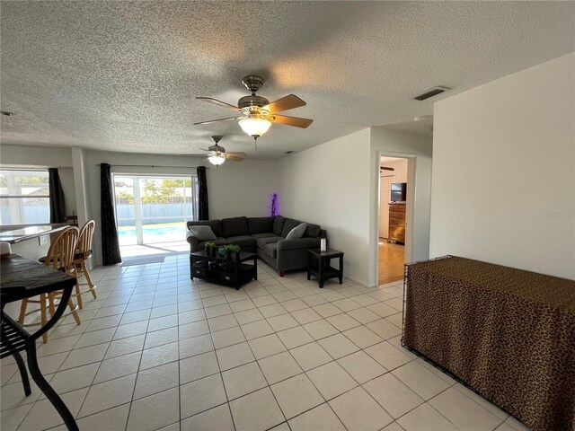 living room with a textured ceiling, visible vents, ceiling fan, and light tile patterned floors