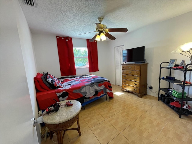 bedroom featuring light tile patterned flooring, visible vents, ceiling fan, and a textured ceiling
