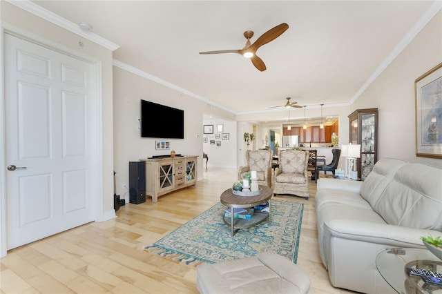 living room with light wood-type flooring, ornamental molding, baseboards, and ceiling fan