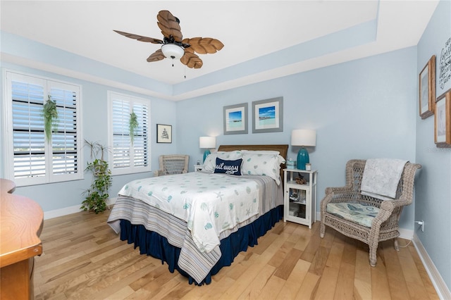 bedroom featuring baseboards, light wood-style flooring, ceiling fan, and a tray ceiling