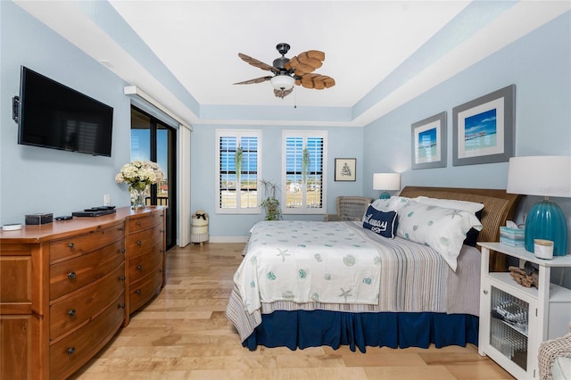 bedroom with access to exterior, baseboards, a tray ceiling, a ceiling fan, and light wood-style flooring