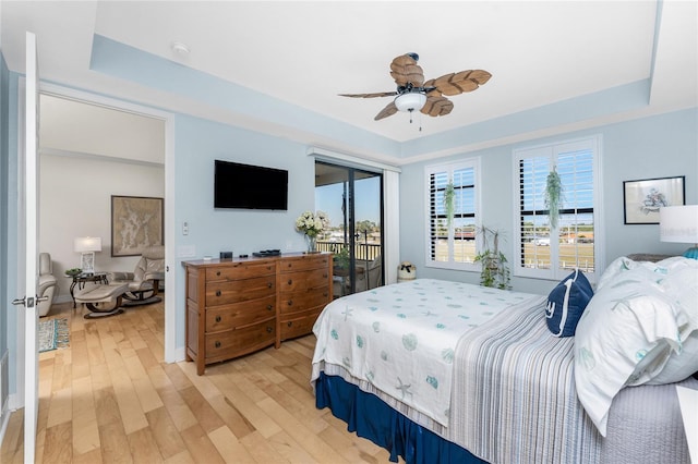 bedroom featuring a ceiling fan, access to exterior, a raised ceiling, and light wood-type flooring