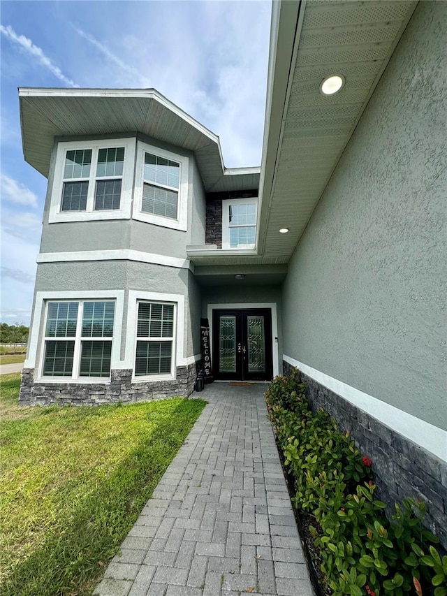 entrance to property with stucco siding, stone siding, french doors, and a yard