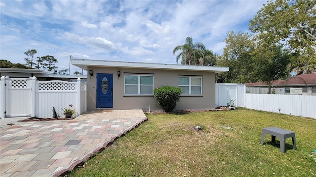 rear view of house with a gate, a lawn, stucco siding, and fence