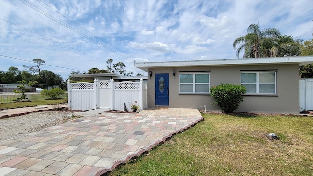 view of front of house featuring stucco siding, a front lawn, fence, and a patio area