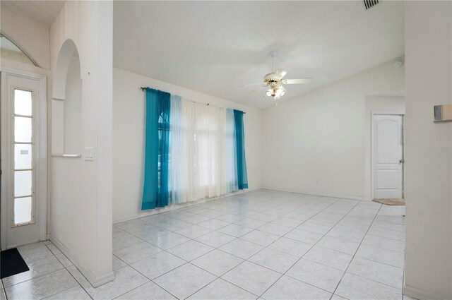 empty room with light tile patterned flooring, a wealth of natural light, vaulted ceiling, and a ceiling fan