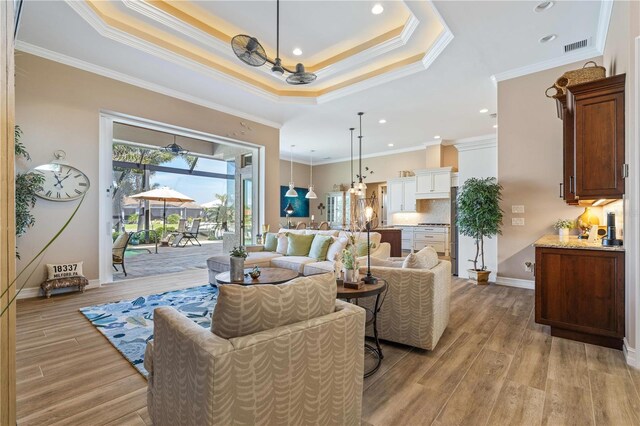 living area with a notable chandelier, a tray ceiling, light wood finished floors, and crown molding