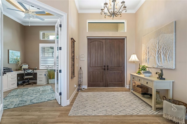 entryway with ceiling fan with notable chandelier, crown molding, baseboards, and light wood-type flooring