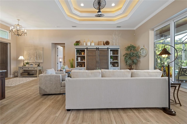 living area featuring light wood-style flooring, a notable chandelier, crown molding, and a raised ceiling
