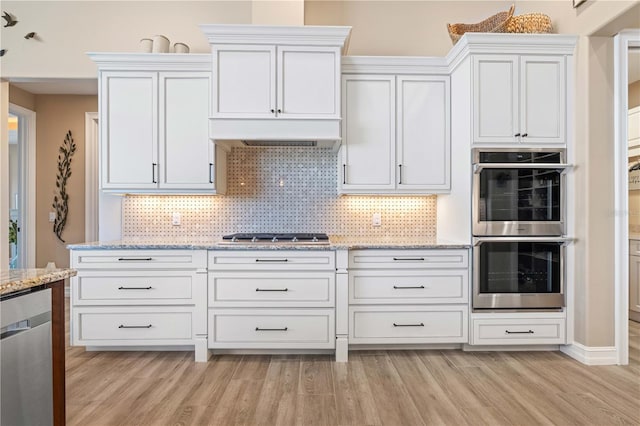 kitchen featuring white cabinetry, light stone countertops, exhaust hood, and appliances with stainless steel finishes