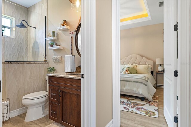 ensuite bathroom with visible vents, walk in shower, toilet, wood finished floors, and vanity