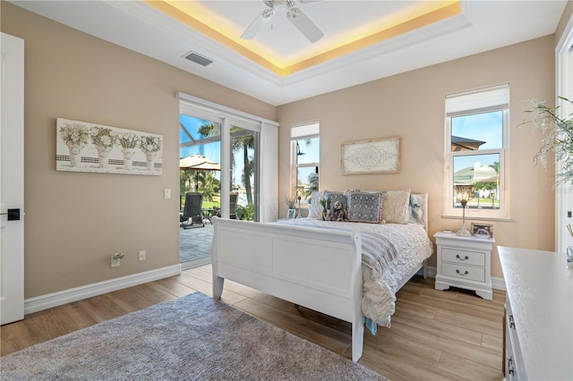 bedroom with light wood-style floors, a tray ceiling, access to exterior, and visible vents