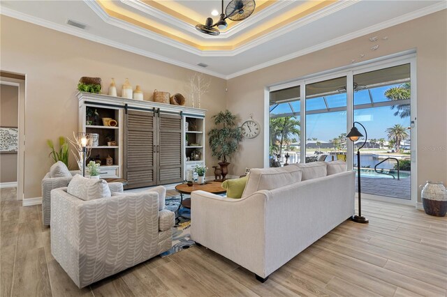 living room with visible vents, crown molding, light wood-style floors, a tray ceiling, and an inviting chandelier