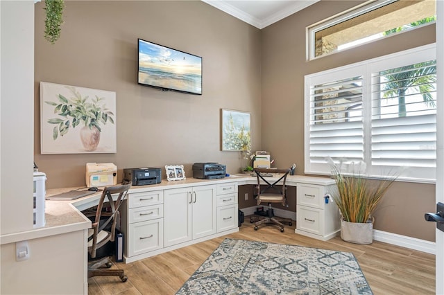 office area featuring light wood finished floors, baseboards, built in desk, and ornamental molding